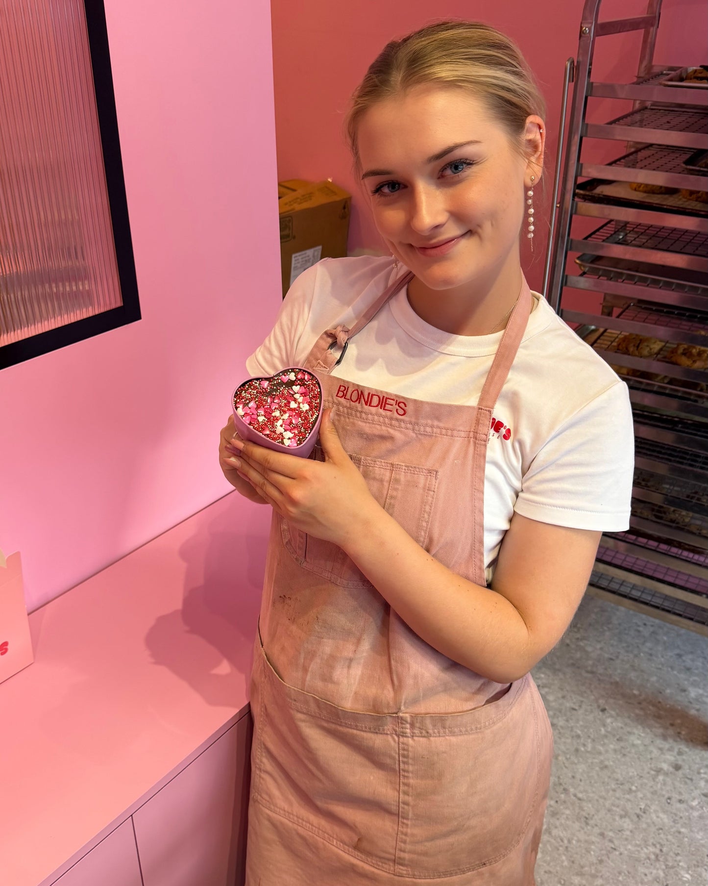Person wearing a pink apron holding a red object in a pink-themed room.