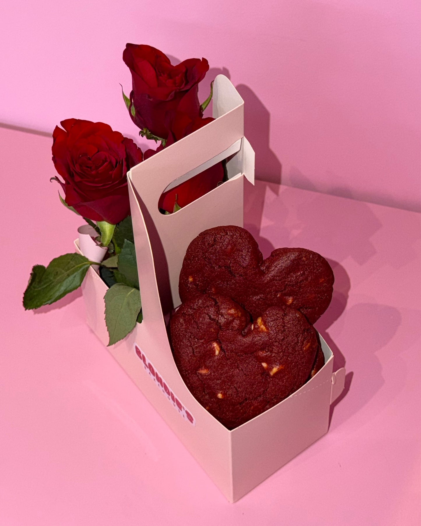 Heart-shaped chocolate cookies in a box with red roses on a pink background